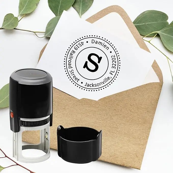 A black self-inking stamp with a circular logo and text is placed on a brown envelope next to a stamp pad.
