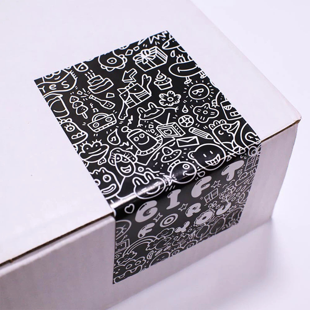 A rectangular box with black and white line art stickers tied with a ribbon, intended for gift packaging.