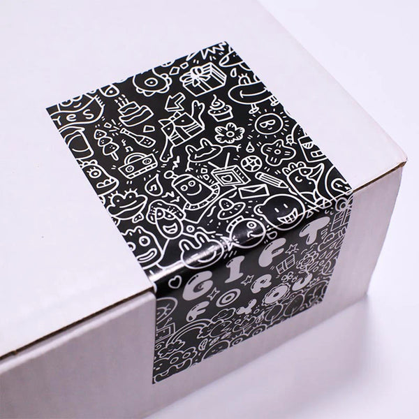 A rectangular box with black and white line art stickers tied with a ribbon, intended for gift packaging.