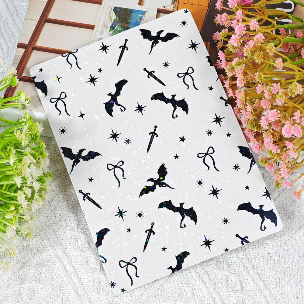 Ein Blatt dekorativer Insertkarten mit schwarzen Fledermaus- und Sternsilhouetten auf weißem Papier, neben rosa Blumen platzi