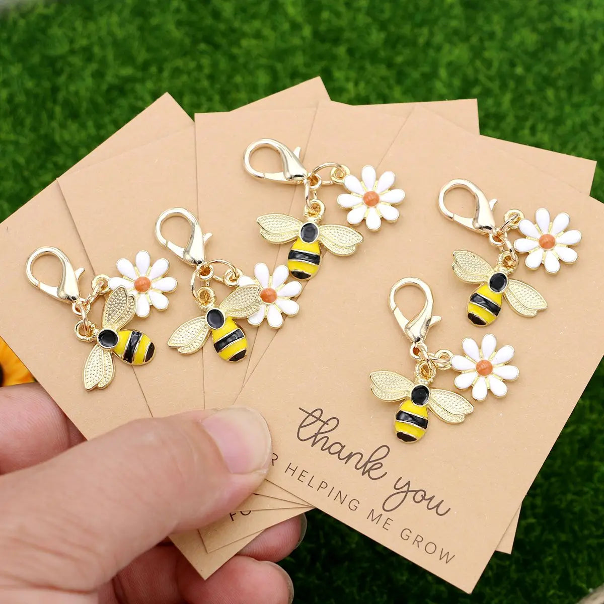 A set of five cute ladybug and daisy keychains is shown on thank you cards against a green background.