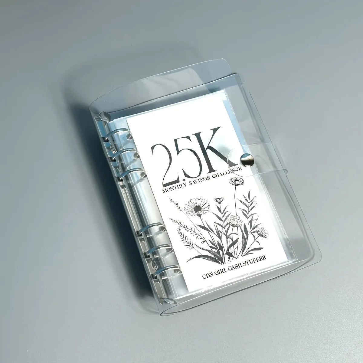 A clear plastic binder set for monthly savings challenges featuring a 25K goal and floral design.