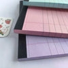 A stack of tearable lined writing pads in shades of pink and purple are shown on a white surface.