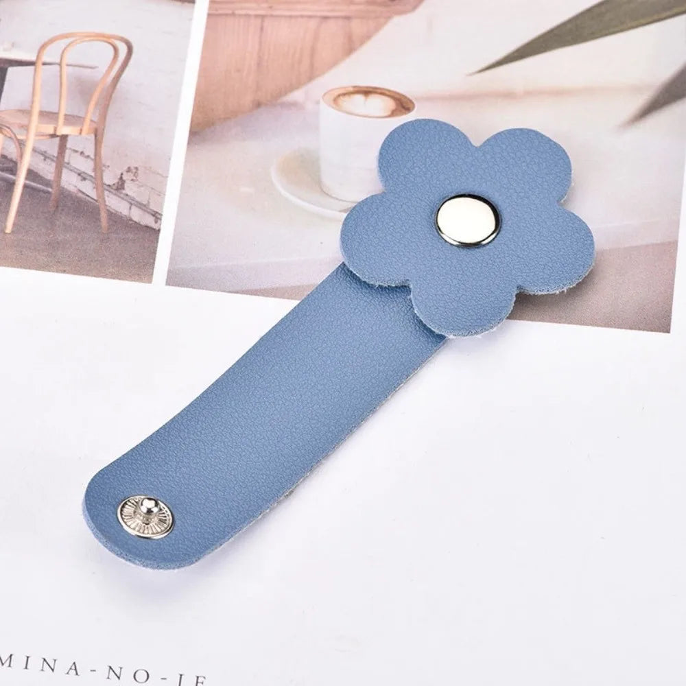 A light blue leather flower cable organizer with a silver button and a small metal stud, shown against a soft background.