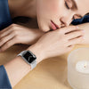 A close-up of a woman's wrist wearing an Apple Watch with a shimmer glitter nylon strap, resting on a wooden surface.
