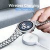 A hand holds a silver Michael Kors smartwatch near a white wireless charging pad.