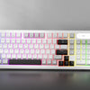 A white membrane keyboard with colorful RGB backlighting is displayed on a dark surface next to a controller.