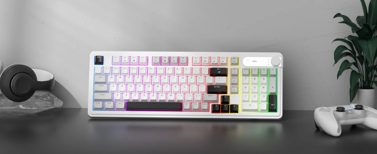 A white membrane keyboard with colorful RGB backlighting is displayed on a dark surface next to a controller.