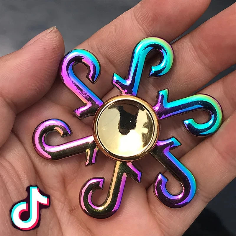 A hand holds a rainbow metal fidget spinner with iridescent blue and purple blades.