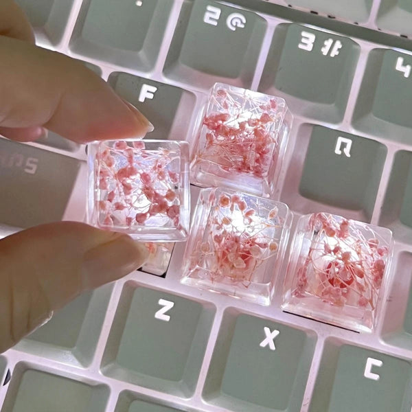 Small translucent pink resin keycaps shaped like botanical elements resting on a light-colored mechanical keyboard.