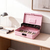 A pink secure metal money box with a hinged lid is displayed on a light wood desk.
