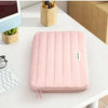 A pink padded laptop sleeve resting on a white desk next to a tablet and wooden containers.
