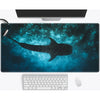 A dark blue ocean scene featuring a silhouette of a whale shark on a mouse pad with a computer monitor and keyboard.