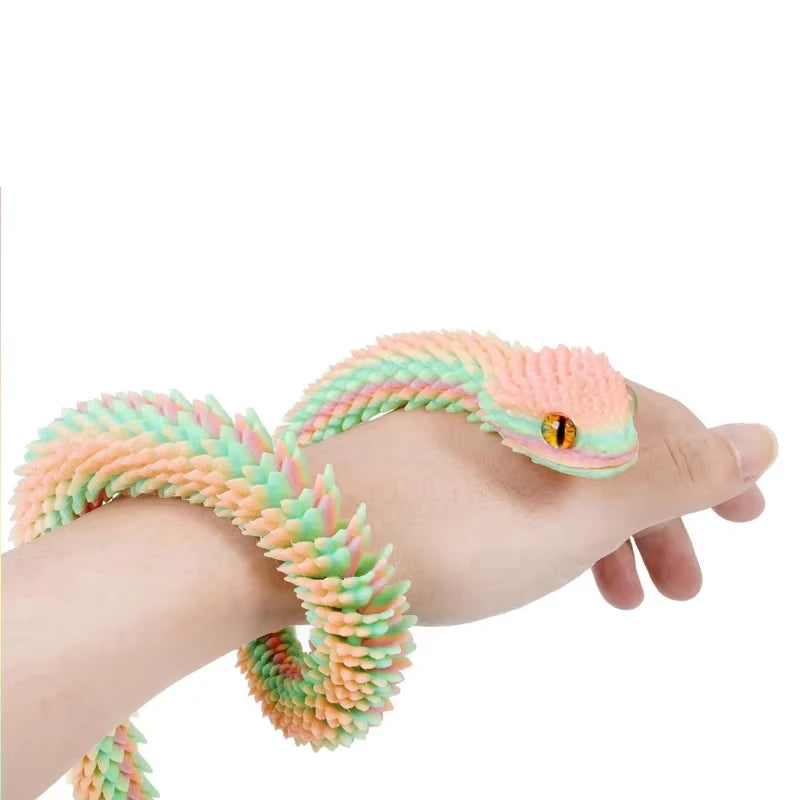 A hand is holding an articulated 3D printed snake figurine with pink and green scales.