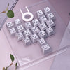Eine Sammlung personalisierter Schmetterlings-Keycaps und eine weiße Ring-Keycap in einer klaren Kunststoffschale.