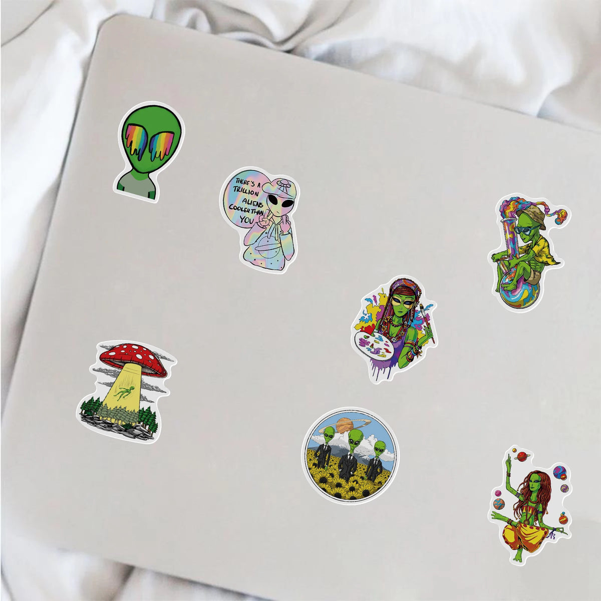 A collection of colorful psychedelic alien and leaf stickers placed on a white laptop.