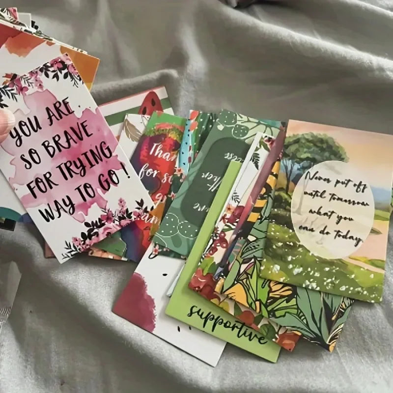 A collection of colorful motivational greeting cards featuring nature and floral designs laid out on a light gray surface.