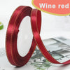 Roll of wine red satin ribbon with gold edge, shown against a blurred background.