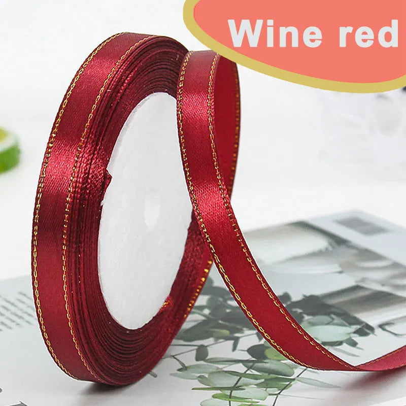 Roll of wine red satin ribbon with gold edge, shown against a blurred background.