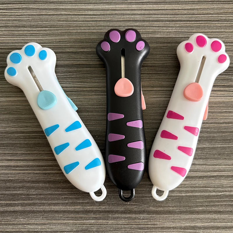 Three colorful retractable cat paw utility knives displayed on a gray wooden surface.
