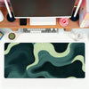 A dark green and beige abstract wave mouse pad placed on a wooden desk next to a laptop and mouse.