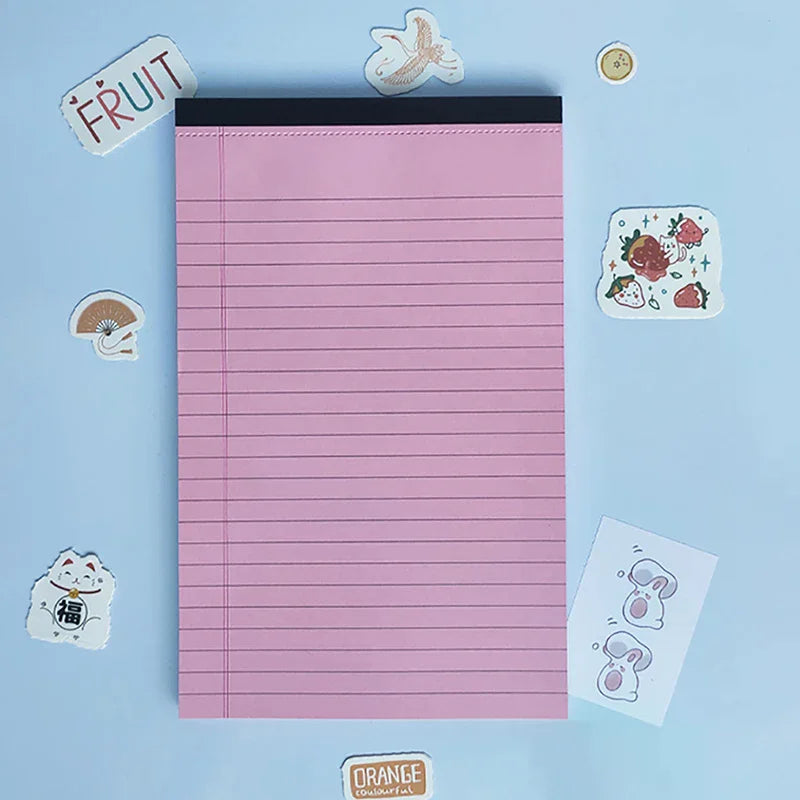 A pink lined writing pad with decorative fruit and food stickers on a light blue background.