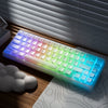 A backlit mechanical keyboard with RGB lighting is shown on a wooden desk next to a white cloud.
