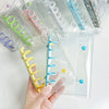 A hand holds a clear double-button colorful binder for stickers and journaling with various colored plastic rings.