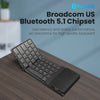 A black foldable Bluetooth keyboard with a touchpad is shown on a wooden desk.