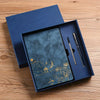 A dark blue luxury PU leather notebook set with a gold embossed landscape design and a black pen inside a navy blue box.