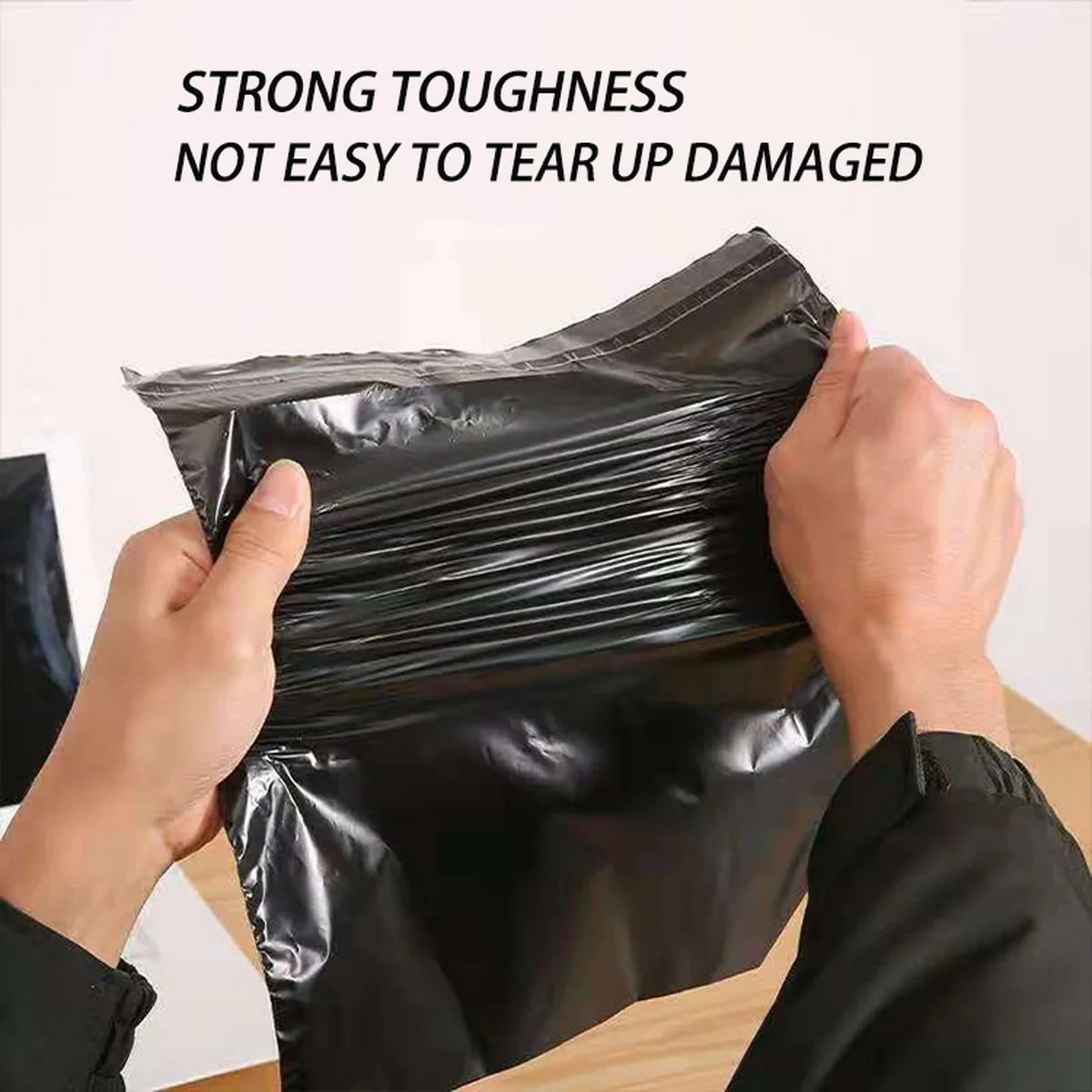 Hände zeigen eine schwarze Poly-Mailertasche, die ihre hohe Zähigkeit und Reißfestigkeit demonstriert.