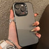 A hand holds a matte gray iPhone with a clear case, featuring gold jewelry and nails.