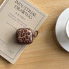 A small, round earphone case covered in a leopard print design rests on a piece of paper with text about industrial drawing.
