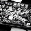 A close-up view of a black and white comic-style PBT keycap set featuring various function keys and symbols.