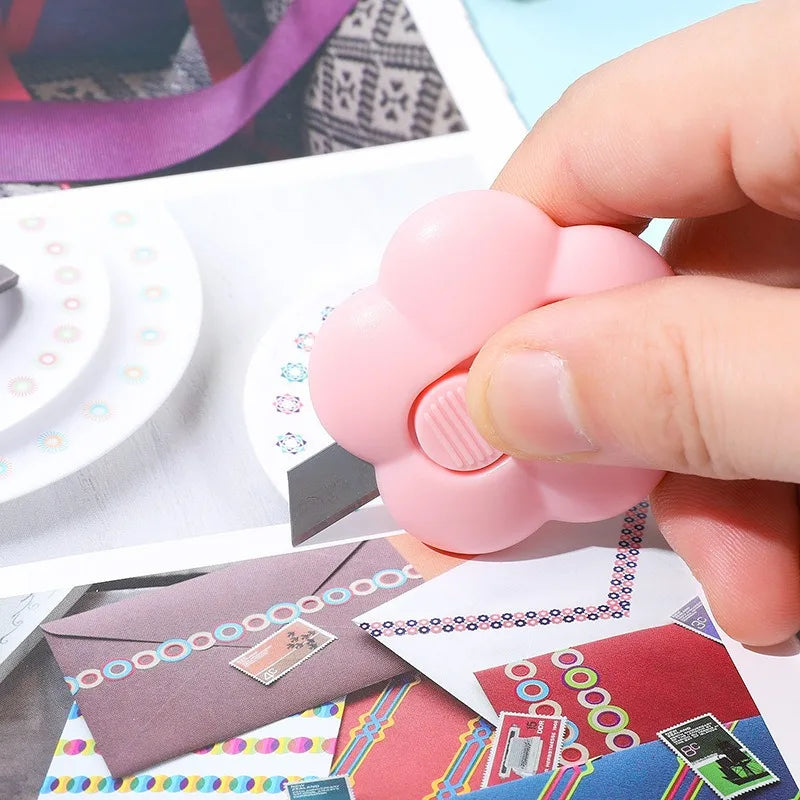A hand holds a pink floral design letter opener and paper cutter next to various colored papers.