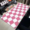 A pink and white checkered desk mat is placed on a wooden desk next to a keyboard and gaming controller.
