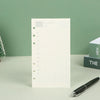 Un cuaderno de hojas sueltas blanco con cuadrícula y líneas numeradas junto a un bolígrafo negro sobre una superficie verde c