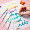 A hand writes 'I will always love my friends and family' on white paper using a set of colorful glitter gel pens.