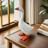 A white resin magnetic duck key holder with an orange beak and feet sitting on a wooden desk.