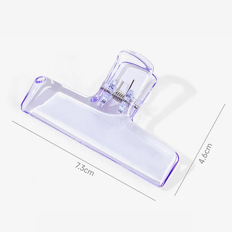 A clear plastic book page clip with a translucent purple tint, showing its size and structure.