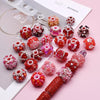 A collection of handmade acrylic flower beads in various shades of pink and red arranged on a white card.