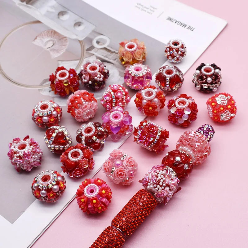 A collection of handmade acrylic flower beads in various shades of pink and red arranged on a white card.