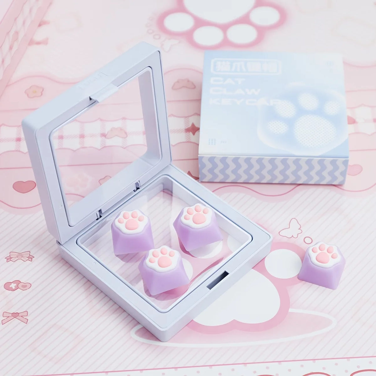 A clear plastic case holds purple cat paw and pink heart keycaps for MX switches on a pink background.