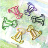 A collection of colorful sitting dog shaped paper clips in various shades of pink, purple, green, and gold on a light green b