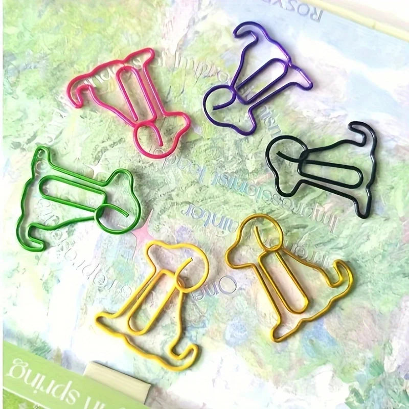 A collection of colorful sitting dog shaped paper clips in various shades of pink, purple, green, and gold on a light green b