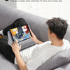 A person is relaxing on a couch watching TV with a tablet held in a stand designed to free their hands.