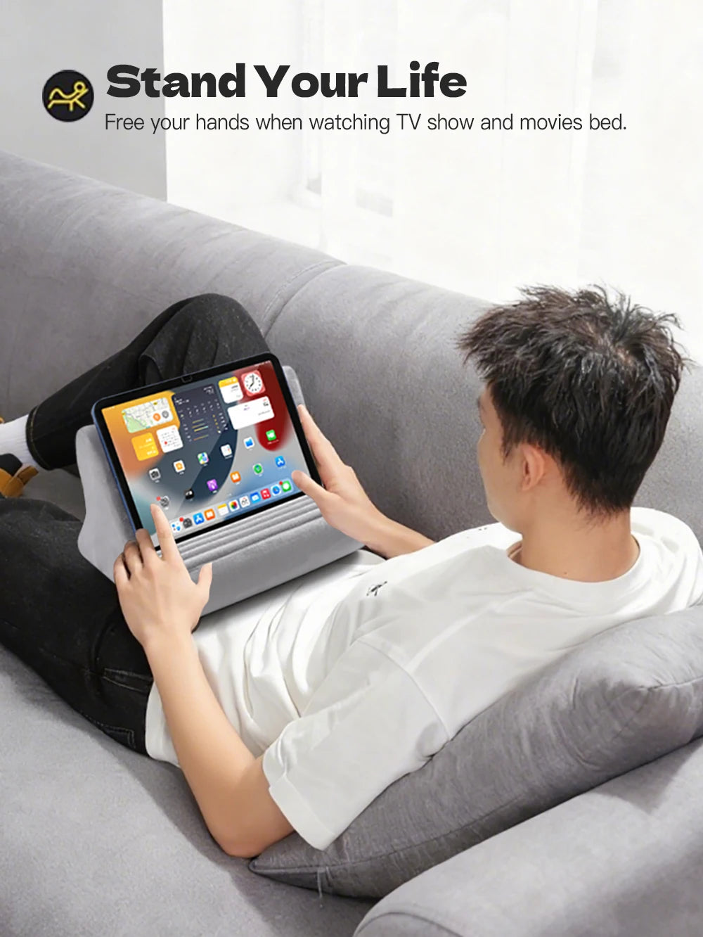 A person is relaxing on a couch watching TV with a tablet held in a stand designed to free their hands.