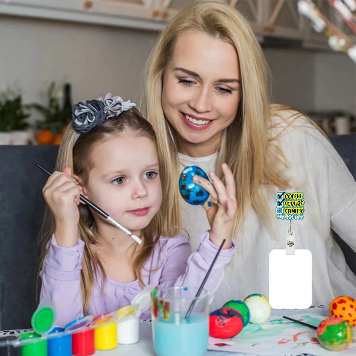 A blonde woman is smiling while a young girl holds a silver badge reel with a glitter acrylic design.