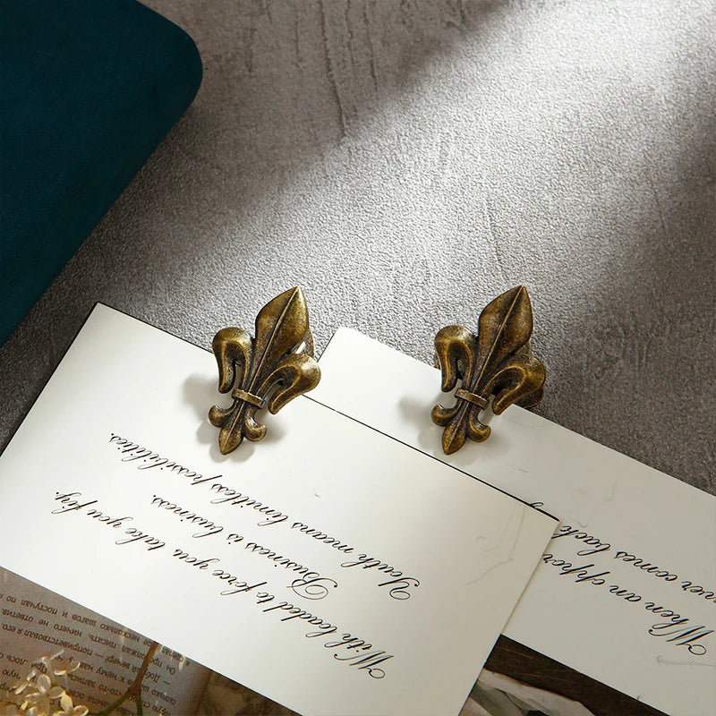A set of two decorative iris-shaped gold metal binder clips resting on a white card against a gray background.