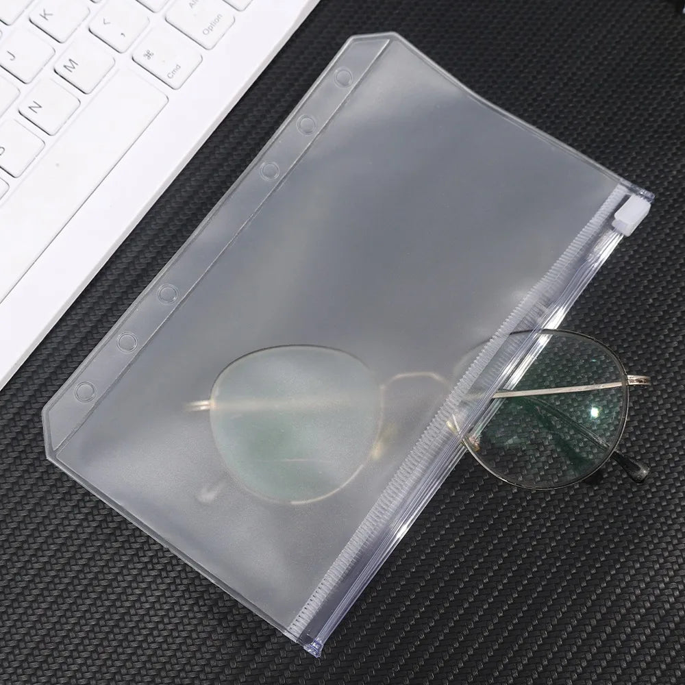 A clear PVC zipper binder pocket containing a pair of eyeglasses, resting on a dark surface.